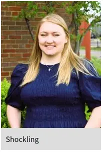 Headshot of Mattea Shockling, woman dressed in a navy blue, standing in front of a brick wall. 