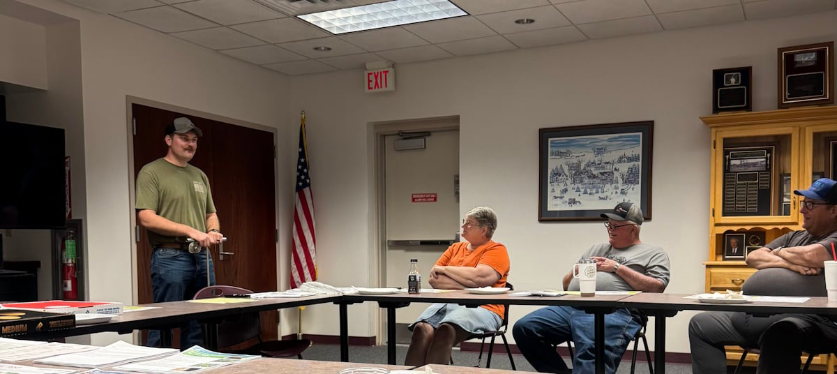 Image of a man standing at the head of a conference room speaking to a group of local community members at a mental health programming event.