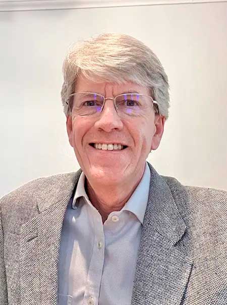 Headshot of a man with white hair wearing eyeglasses, a light blue button up and a grey tweed sport coat.